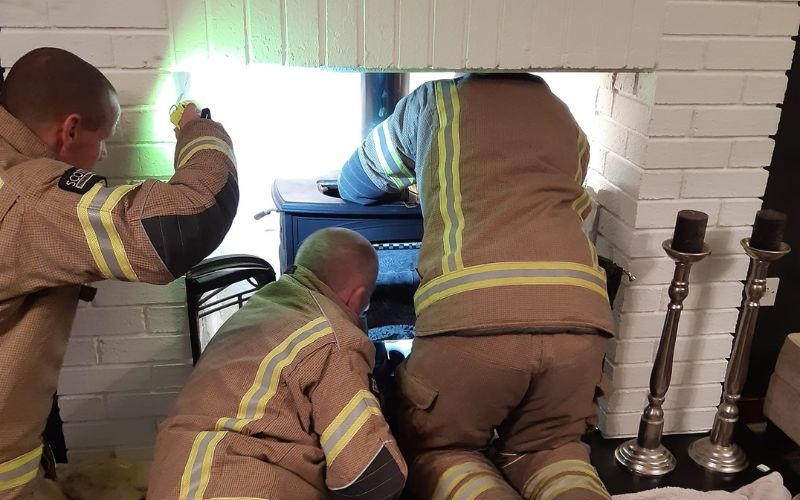 three members of Scottish fire and rescue service look up the chimney of a wood burning stove with a torch