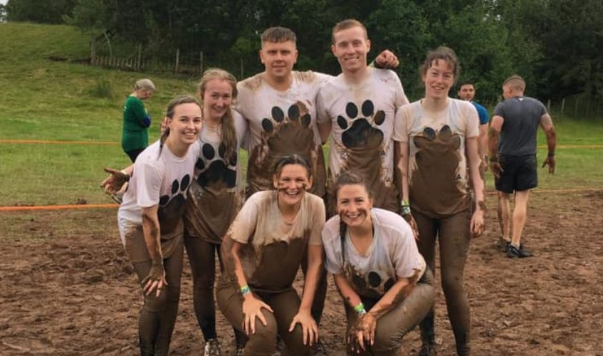 team wearing Scottish SPCA t-shirts covered in mud in muddy field