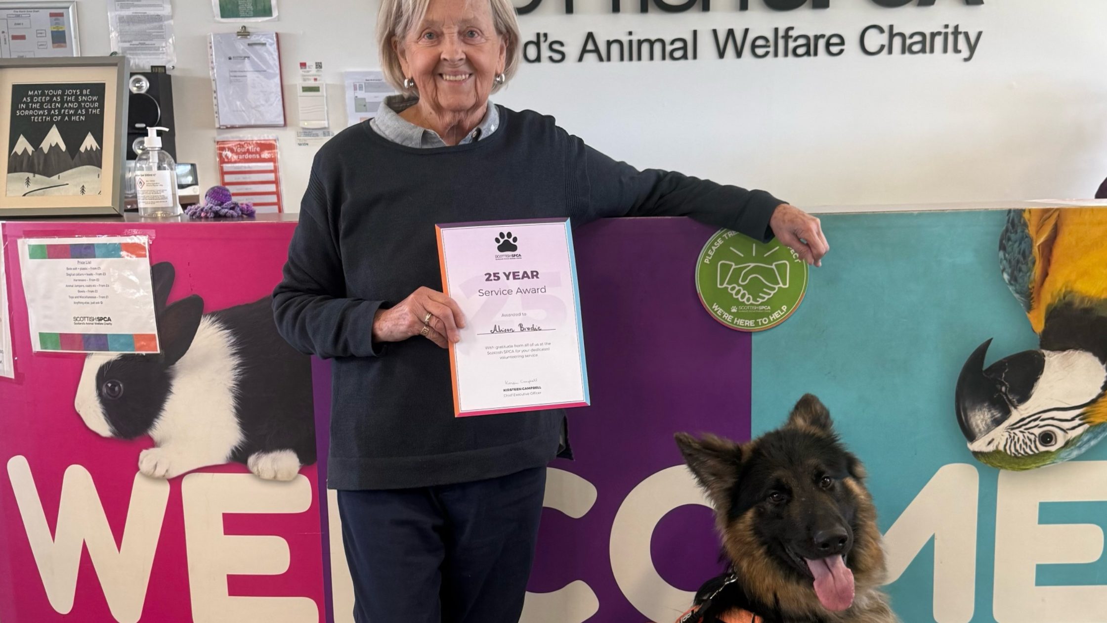 Photograph of volunteer Alison holding certificate with german shepherd by her side